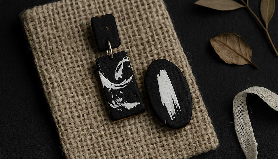 Bijoux en liège noir et blanc sur tissu brut, entourés d’éléments naturels. Équilibre entre style et écologie signé Paola Borde